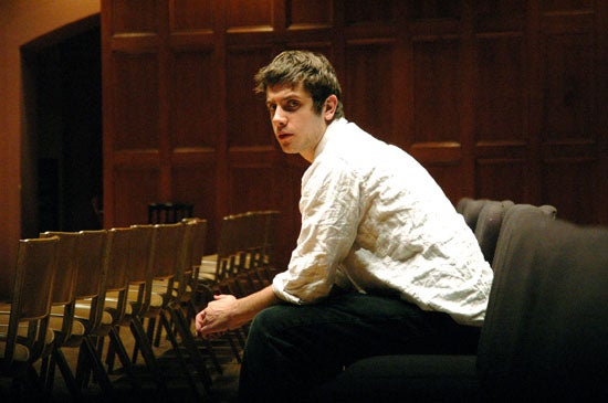 Professional photo of Andrew sitting amidst chairs meant for an audience looking toward the camera