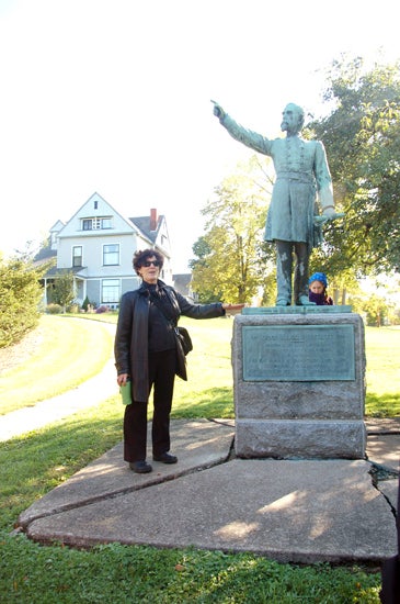 A professor standing in front of a statue of a man pointing out of view