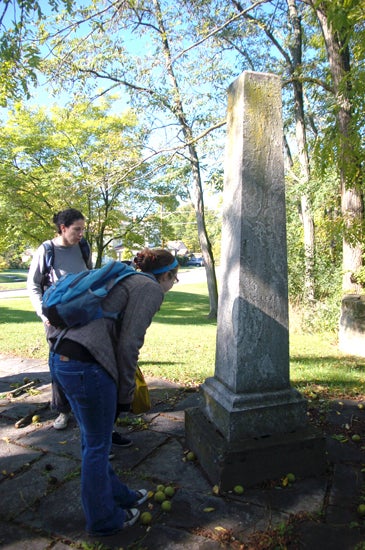 Two students looking at a memorial. The memorial is taller than both of them and is shaped lie a pillar