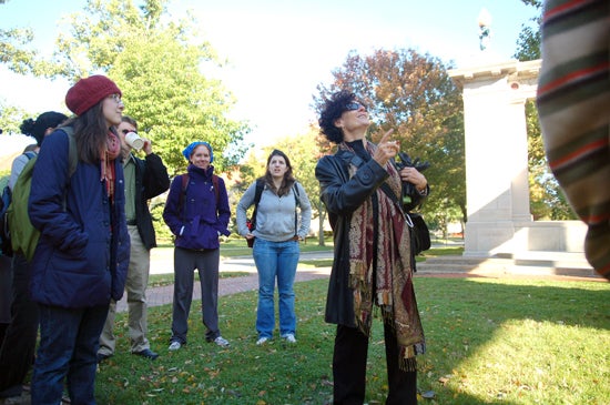 A professor pointing at the arch. A group of students stand around and listen