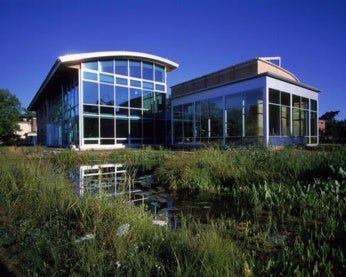 Modern, glass-walled building surrounded by lush vegetation