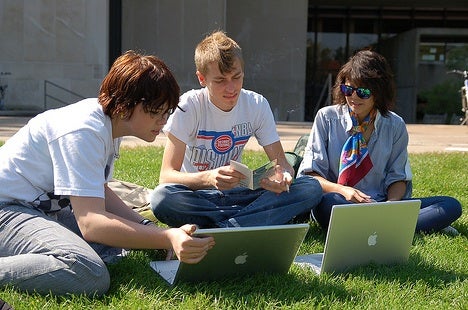 Three students in the grass looking at their computers 