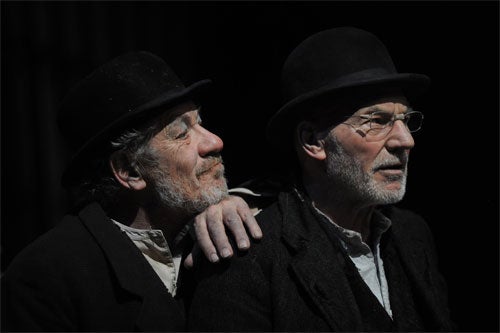 Two actors wearing black top hats and blazers. One has his hand resting on the other's shoulder with his chin propped up on his hand.