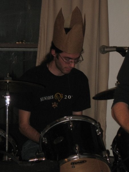 A boy playing the drums wearing a paper crown