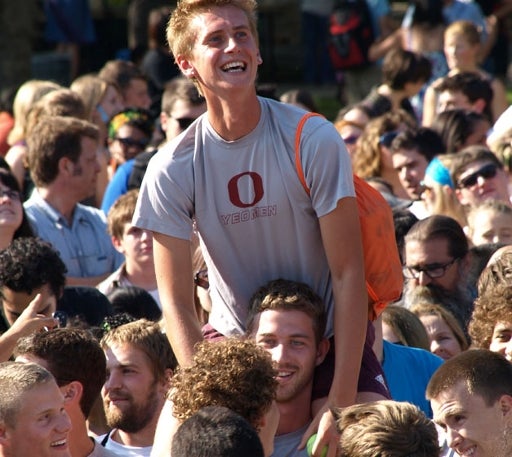 A young man sits on his friend's shoulders to see above the crowd.