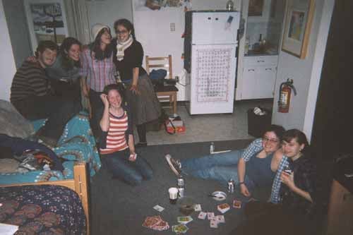 A group of 7 playing cards in a dorm room with a kitchen.