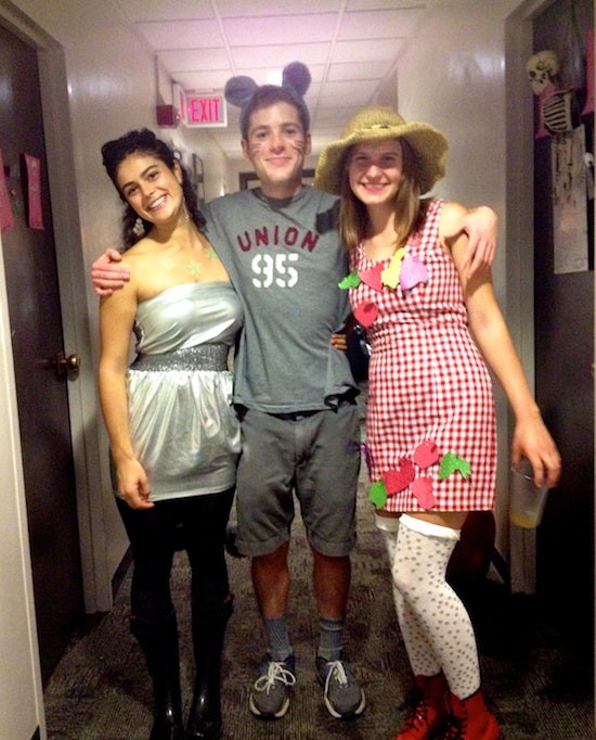 A boy dressed in all gray with mouse ears has his arms around Georgia, who is wearing a silver dress, and another friend who is wearing a checkered dress