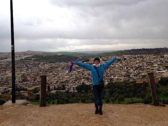 Georgia posing for a photo with her arms raised above her head in front of a large cityscape