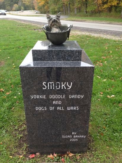 A large tombstone with a stone dog on the top. Engraved: "Smoky: Yorkie doodle dandy and dogs of all wars"