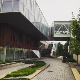 a modern glass building has a walkway extending over a walking path