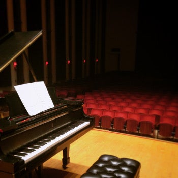A piano on stage in an empty hall.