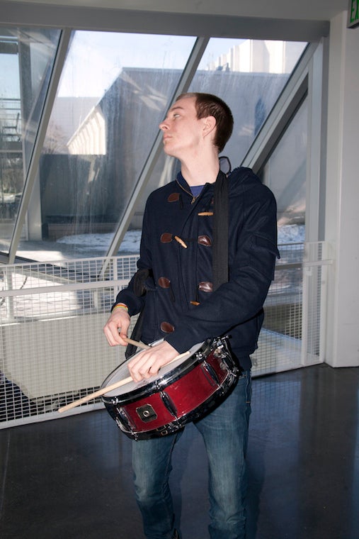 A student drums on a drum hanging around his neck