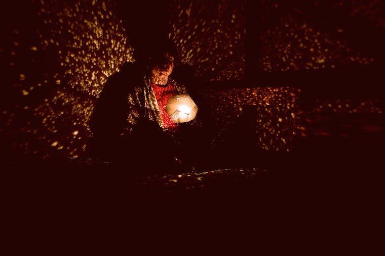 Student sitting in a dark room holding a light that emits light specks 