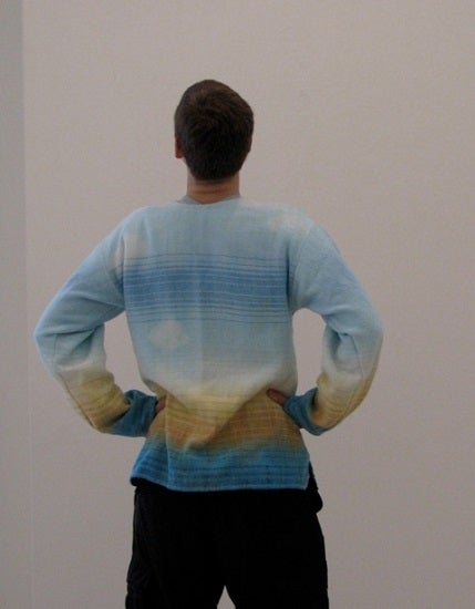 The author with their back to the camera, hands on their hips, and head tilted upward looking at a blank white wall 