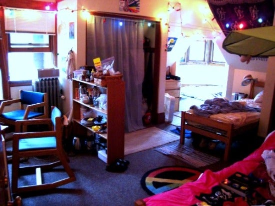 The inside of the room. Pictured is a bed, chairs, a closet, and overhead lights
