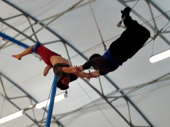 Two circus performers mid air holding each others arms