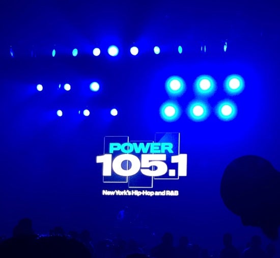 A performance space lit by stage lights. A graphic overlay says Power 105.1, New York's Hip-Hop and R&B.