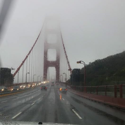 A view of the golden gate bridge taken from a car that is about to cross it. Fog and rain make it difficult to see past the first pillar 