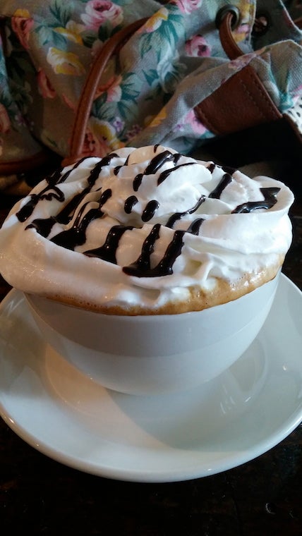 Cup of coffee topped with cream and drizzled with dark syrup