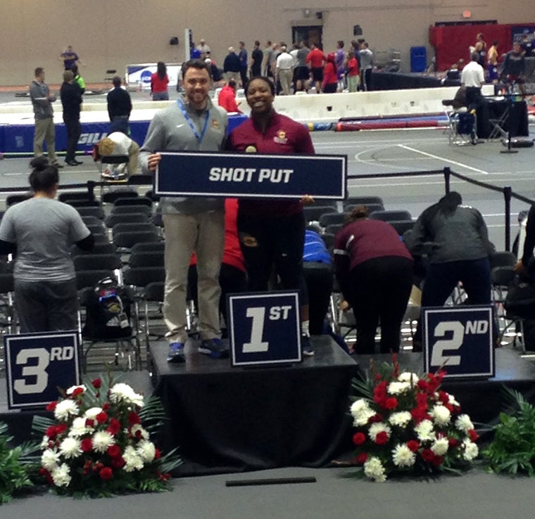 A man and a woman stand on the first place podium holding a sign that says 'shot put'.
