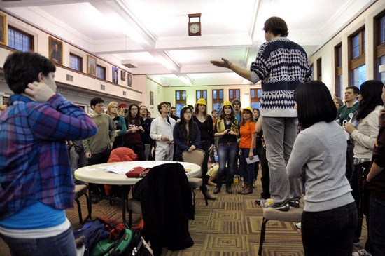 A student stands on a chair and speaks to a crowd