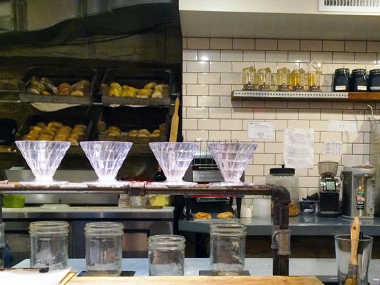 The counter at The Local. Drip coffee makers and Ball jars line the counter. Behind the counter is boxes full of bagels. 
