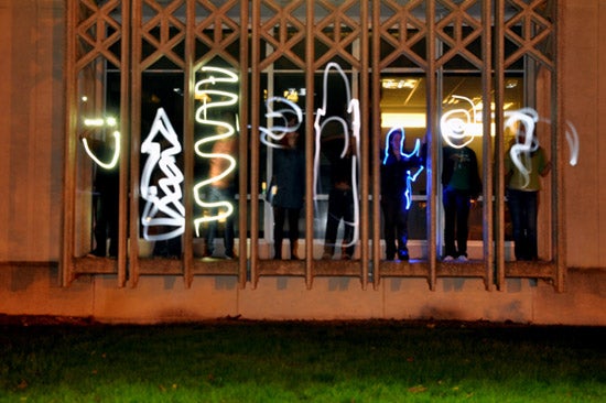 Students stand in a window and makes shapes with light