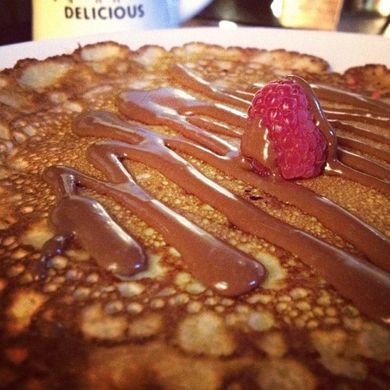 A close up of a pancake drizzled with nutella and one single raspberry