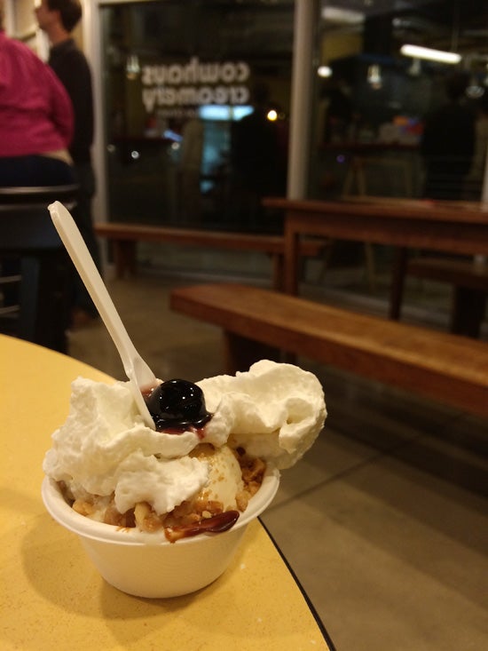 A small bowl of ice cream topped with whipped cream and a syrupy cherry at Cowhouse Creamery 