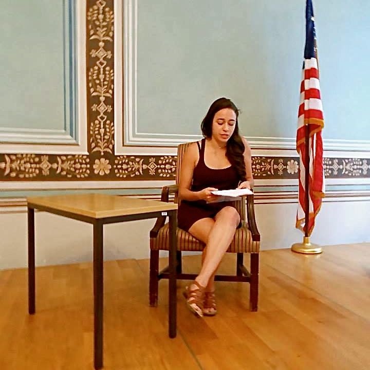 Student sitting in a chair next to an American flag reading 