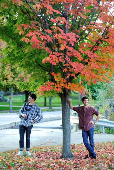 Students leaning against a tree with red leaves