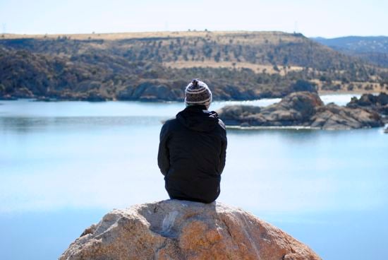 Someone sits on a rock overlooking water 
