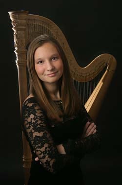 A professional photo of a student with her arms crossed looking at the camera. Behind her is a harp