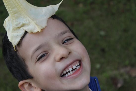 A boy smiles and looks up at the camera with an open flower resting on his head