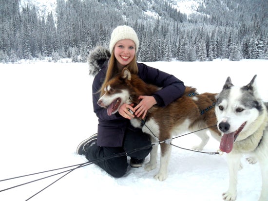 A student smiles for the camera and pets a husky