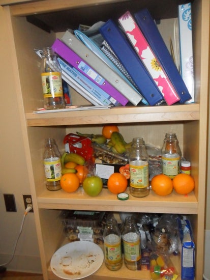 A shelf full of tea bottles, apples, and oranges