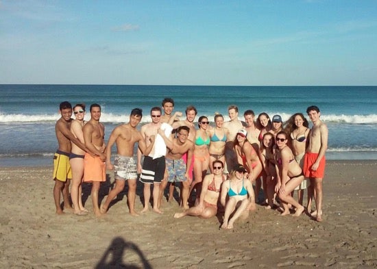 A large group of students wearing beach swim gear posing in front of the ocean