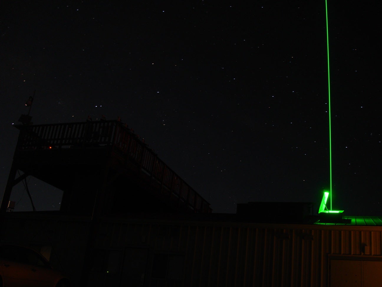 A starry sky with a green laser shining up 