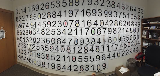 Pieces of paper with numbers on them lining a wall to make up the number pi
