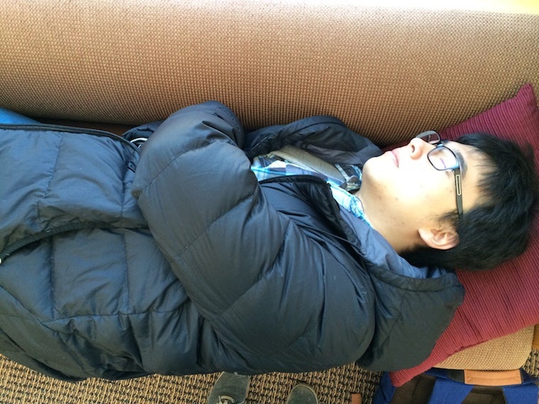 Chul is sleeping peacefully on a couch, still wearing a winter coat and glasses.