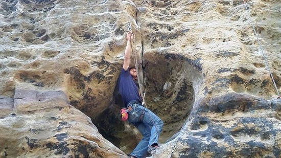A climber unhooks a carabiner from a natural wall 