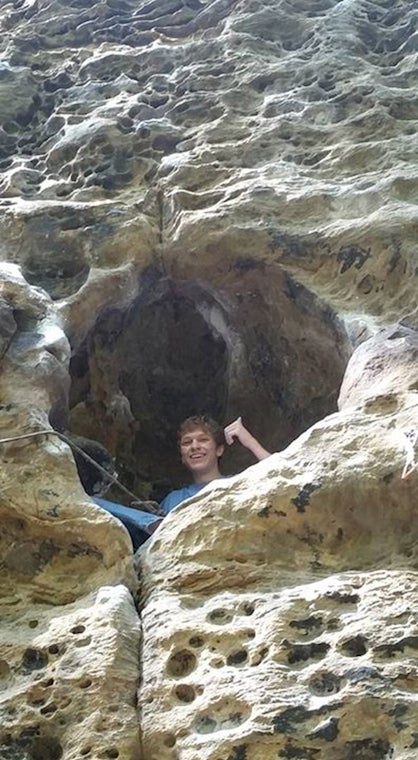 A climber inside of a small cave in a natural wall making a thumbs-up sign 