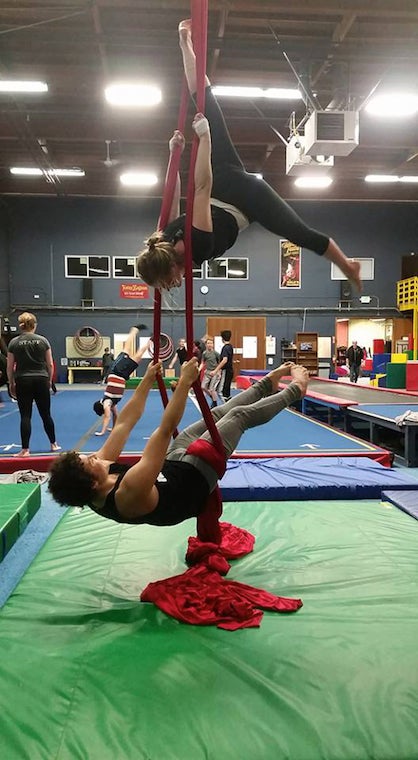 Two aerialists performing on the same hanging cloth in a room full of mats