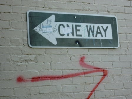 A one way sign with an arrow drawn underneath pointing the opposite way