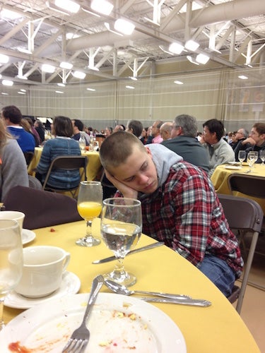 The authors brother sitting at a table filled with empty breakfast food plates. He has his head in his hand and looks unhappy.