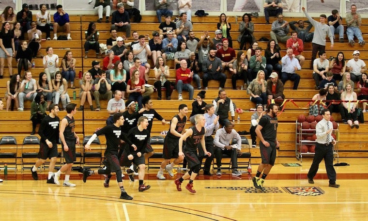 Players on the sideline cheer and run toward the basket at the end of the game