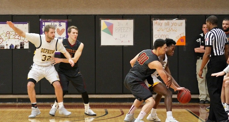 An in action shot of the boys basketball team during a game. The opposing team, Depauw, has the ball and an Obie is defending
