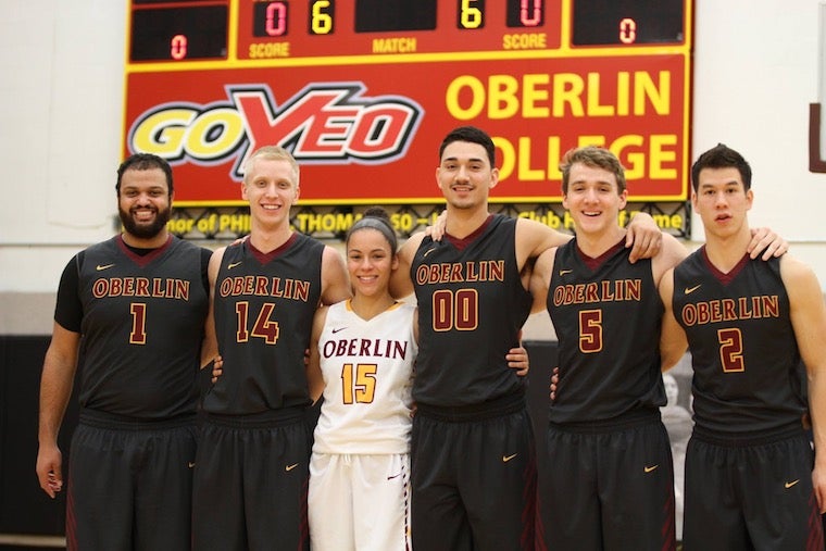 A group of basketball players pose with their arms around eachother in their uniforms