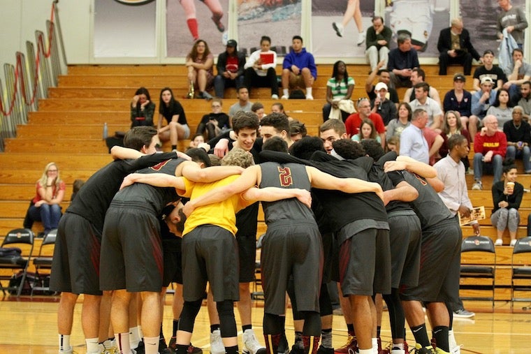 The boys basketball team in a circle with their arms wrapped around each others backs during a game