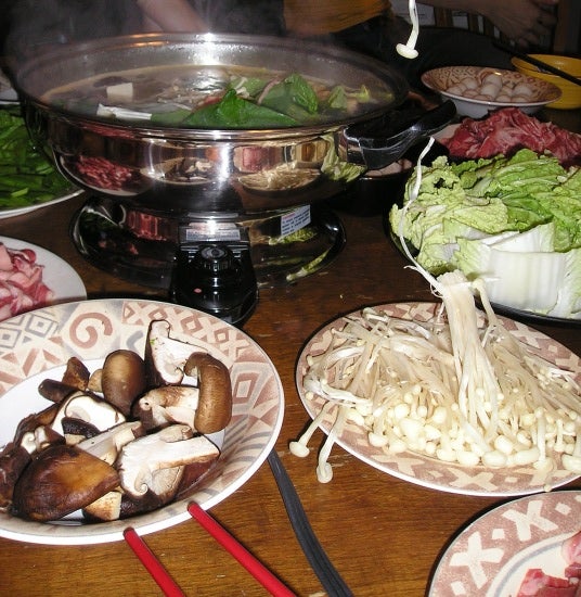 A hot pot with a leafy soup. A bowl of mushrooms. Chopsticks.